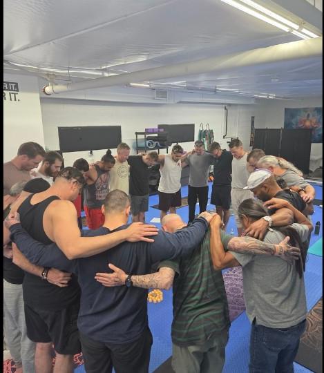Men standing in a circle with arms around each other at a Male Compass gathering